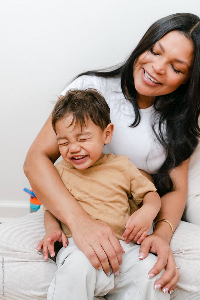 A mother smiling and sitting with her child laughing in her lap.