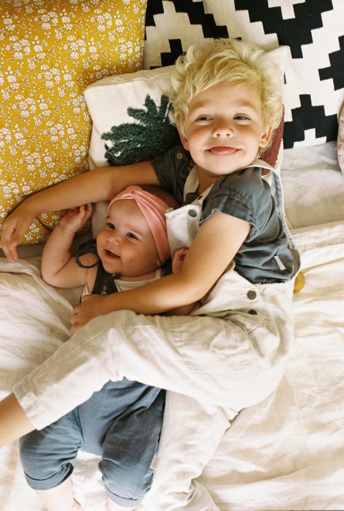 A young boy lying down and embracing his baby sibling, both smiling and looking happy.